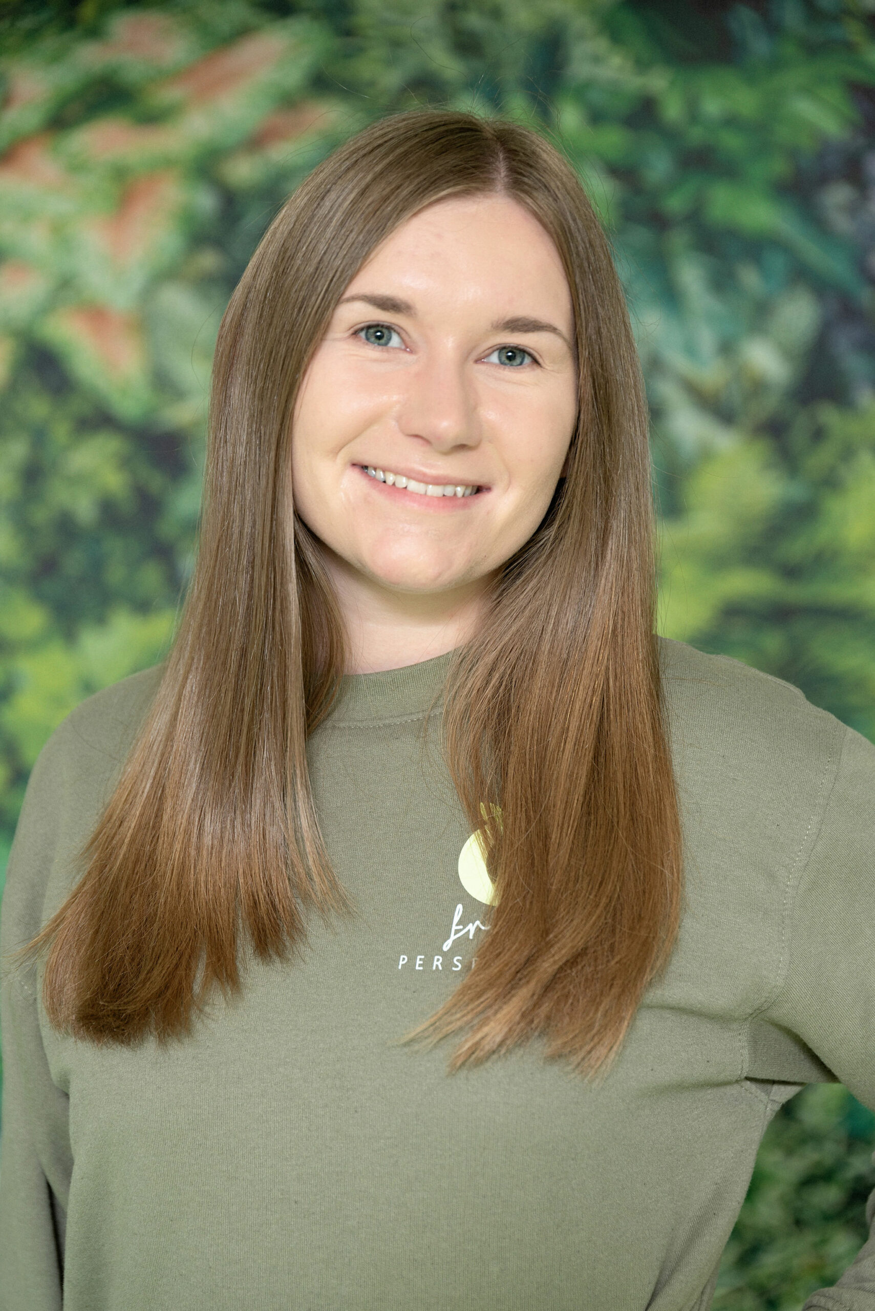 Meet The Team - Fresh Perspective Team Lead Andrea stood with a green jumper on in front of a leaf wallpaper