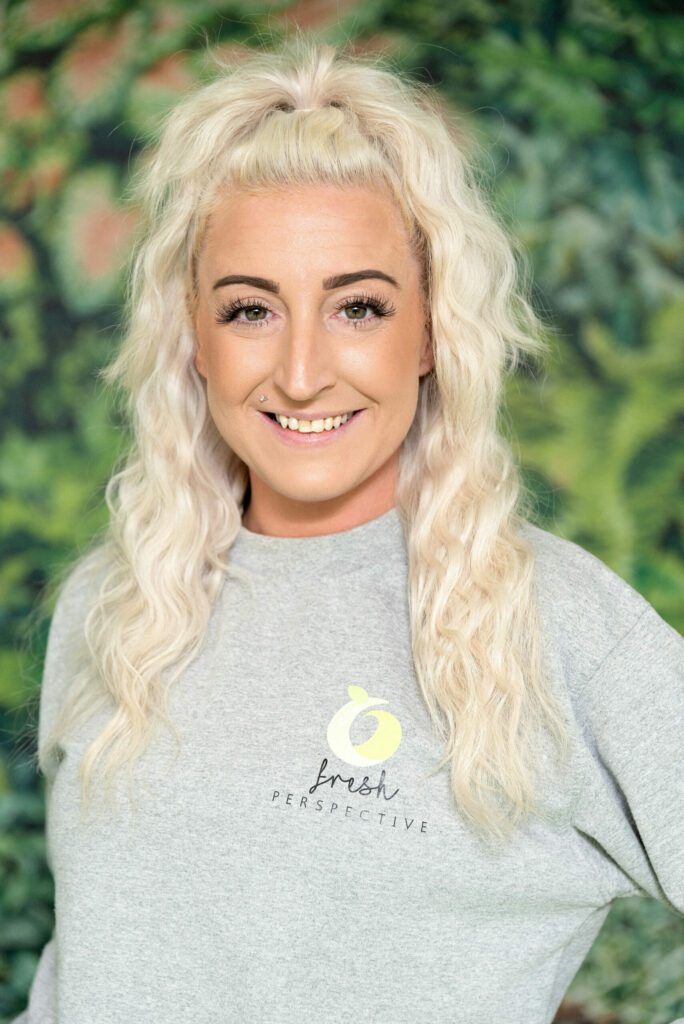 Meet The Team - Fresh Perspective Team Lead - Cheryl stood with a Grey jumper on in front of a leaf wallpaper