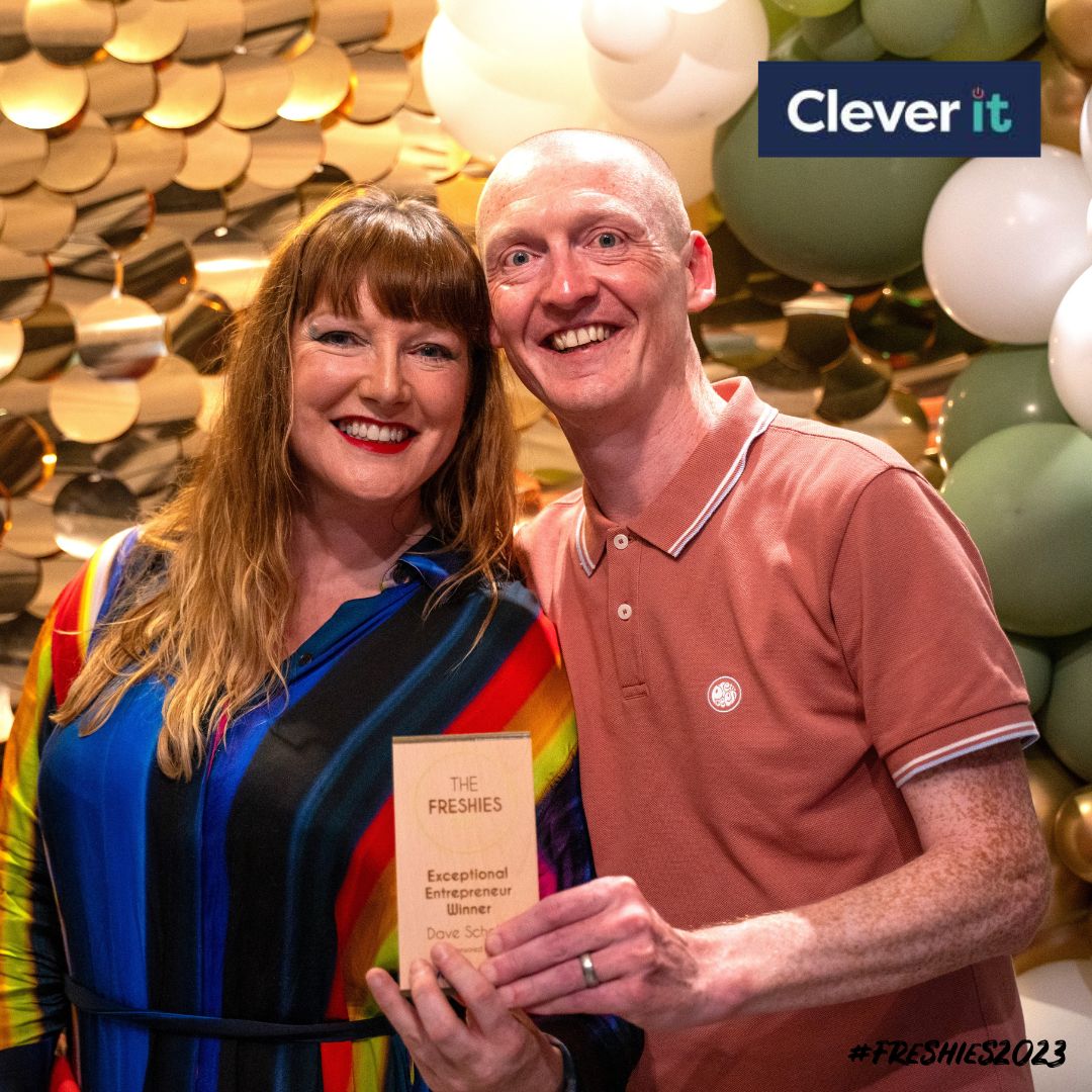 The Exceptional Entrepreneur winner Dave Scholes stood in front of a sparkle background and balloons holding his award along side his colleague Andi Lewis.