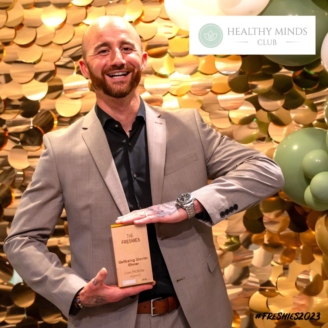 The Wellbeing Warrior winner Liam McBride stood in front of a sparkle background and balloons holding his award.